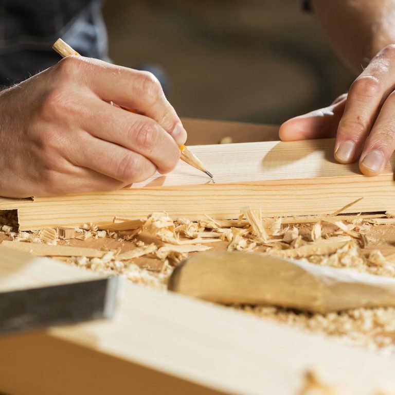 A person marking wood on a workbench surrounded by wood shavings.