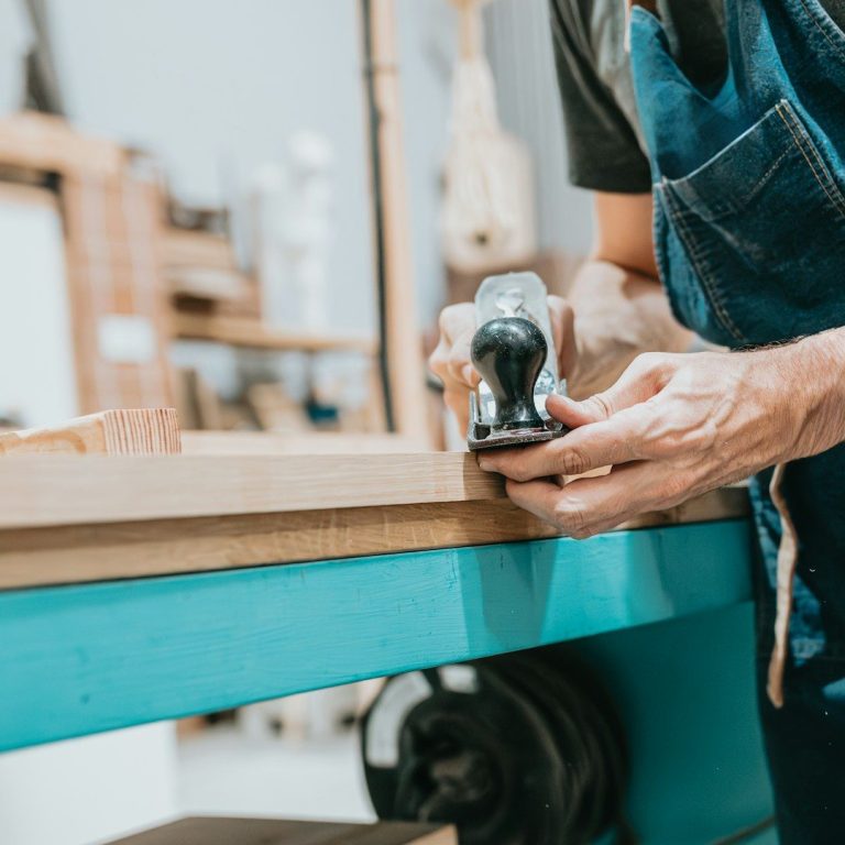 A person using a hand planer on a wooden surface in a workshop setting.
